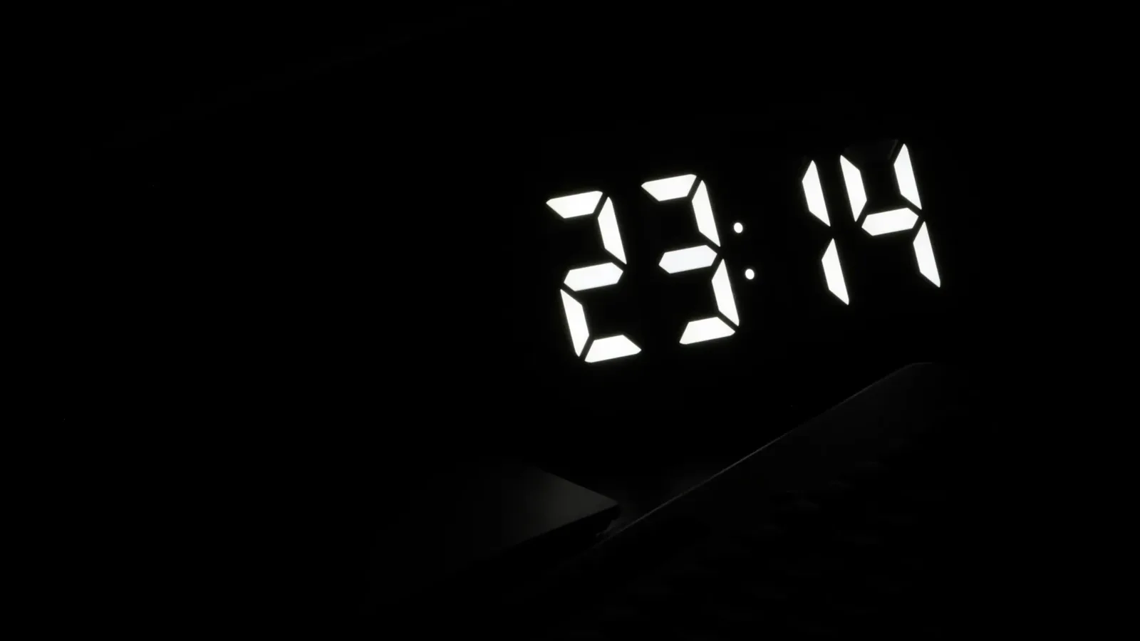 A digital clock glowing in a dark bedroom late at night